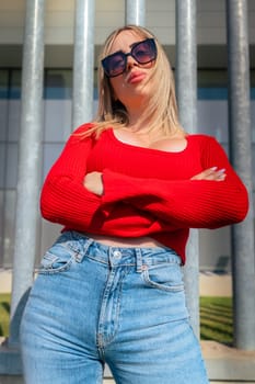 Young woman with sunglasses standing looking surprised and with arms crossed at the camera.