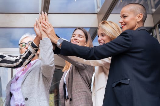 Five happy multiethnic women stacking hands in the city looking at camera