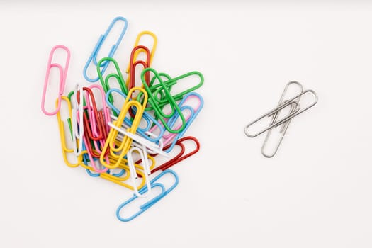 A concept photo of a stack of multi-colored paper clips separate from two plain metal paperclips.