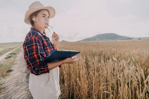 A young woman wearing a hat and plaid shirt looks thoughtfully at a wheat field.