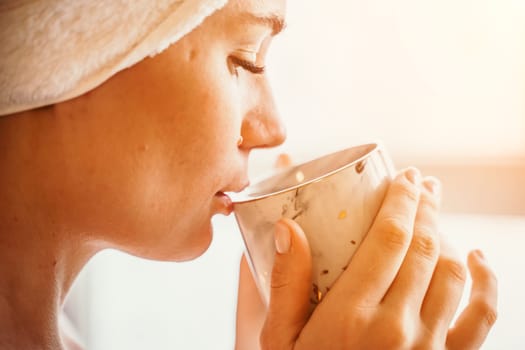 Young serene relaxed woman in spa bath towel drinking hot beverage tea coffee after taking shower bath at home. Beauty treatment, hydration concept