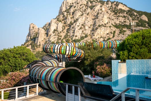 A colorful water slide winds down a cliffside towards a pool, with a mountain in the background. family vacation concept