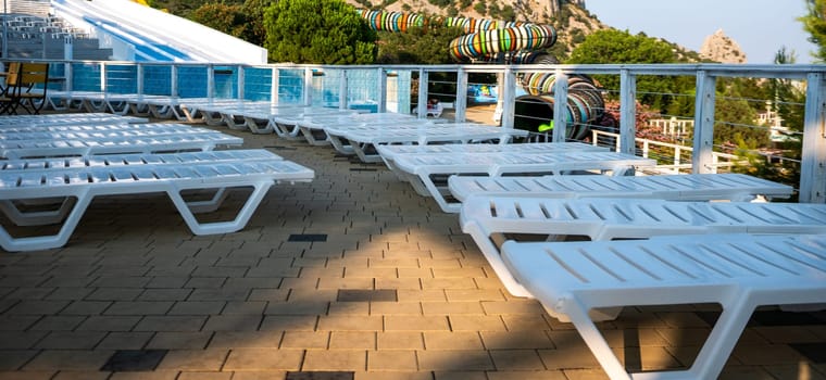 A row of white lounge chairs are lined up on a patio. family vacation concept