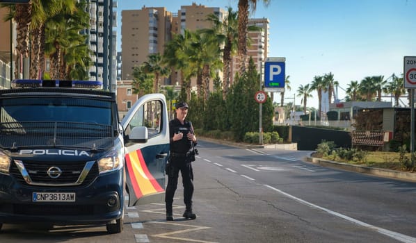 Spanish police officer by van in the city under a sunny sky, with urban buildings and palm trees backdrop, performing traffic duties or conducting a checkpoint download image