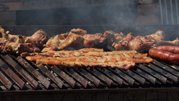 Close-up video of various meats sizzling and smoking on a barbecue grill over hot coals outdoors on a summer day.