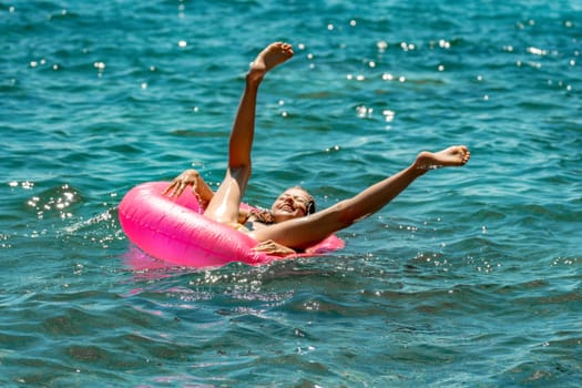 A person in a pink inflatable ring is floating in the ocean with their legs raised in the air.