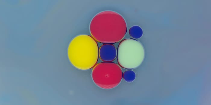 A vibrant collection of spherical shapes in red, yellow, blue, and green floats gracefully against a soft blue backdrop. The colors create a striking visual contrast and harmony.