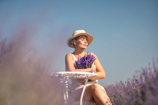 A woman is sitting in a field of lavender flowers and wearing a straw hat. She is smiling and holding a bouquet of flowers. Scene is peaceful and serene, as the woman is surrounded by the beauty of nature.