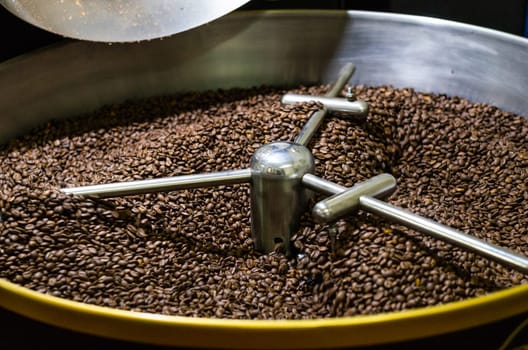 Freshly roasted coffee beans from a large modern coffee roaster are stirred in the cooling cylinder