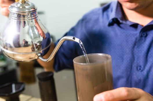 Close-up of a male pouring water into a cup for a hot beverage preparation