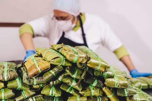 Stack of tamales with unrecognizable woman in the background preparing the Peruvian tamales