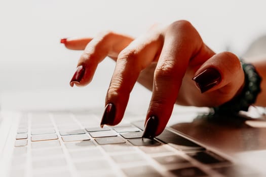 A hand with dark red nail polish types on a laptop keyboard.