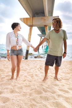 Happy couple in love holding hands and looking at each other at the seashore. A man and a woman are walking on the sand near the ocean. Vows and promises by the sea.