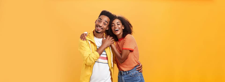 Friends always cover each other. Stylish and carefree loving african american girlfriend hugging boyfriend and smiling broadly touching guy palm hanging around and spending time great together.