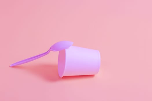 Paper disposable glass and plastic spoon on a pink background. Disposable tableware concept.