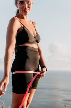 A woman is holding a pink tape measure around her waist. She is wearing black pants and a black top