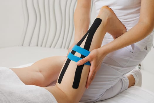 Kinesio taping of the lower extremities to prolong the massage effect close-up, the therapist applies tape to the patient's legs