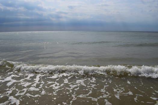 Beautiful landscape - turquoise colored sea water, sand, sky. The waves are on the sea to the shore. The Beach And Splashing Waves