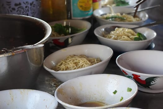 A close-up shot of Tukang Mie Ayam or a noodle vendor preparing multiple servings of chicken noodle soup.