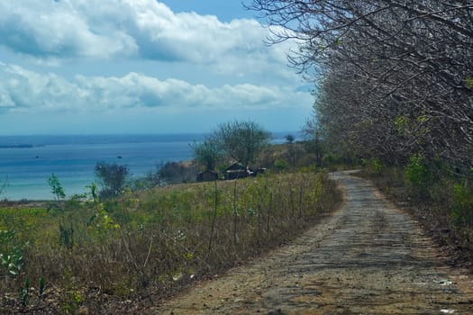 Serene dirt road winds through a grassy hillside overlooking a calm ocean and distant islands near Lombok, Indonesia