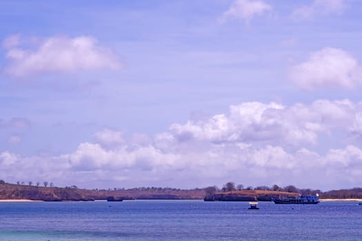 scene of a pristine beach near Pink Beach in Lombok, Indonesia. Clear turquoise waters lap against the white sandy shore, while colorful fishing boats bob gently in the bay