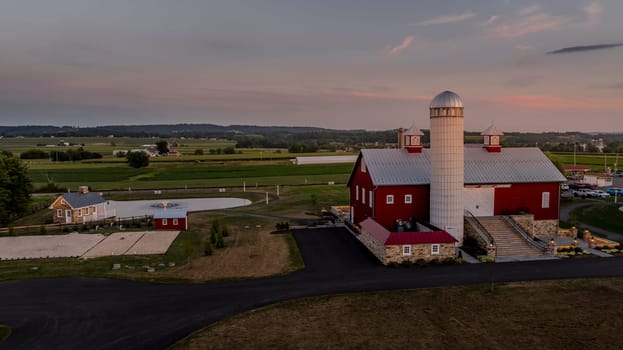 Ronks, Pennsylvania, USA, July 19 2024 - Peaceful Farm Scene At Dusk Featuring A Prominent Red Barn And Tall Silo, A Small Pond With A Fountain, Surrounding Fields And Buildings, And A Winding Road Leading Through The Property