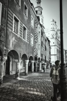 A dramatic black-and-white image capturing the timeless charm of a cobblestone street in Warsaw Old Town. The photograph highlights the beautiful arches and historic buildings, with the distant spire adding depth to the scene. The monochromatic tone evokes a sense of nostalgia and history, reflecting Warsaw resilient past. Perfect for use in themes related to architecture, history, and urban photography.