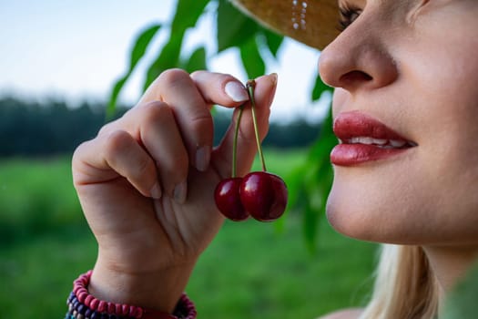 The close-up image captures the essence of a woman's face and hands, revealing her painted, full lips. She is holding red cherries. Her gaze is directed towards the sky, framed by a backdrop of a cherry tree branch and a blurred forest in the distance. Imperfections adorn her skin, adding a raw authenticity to her presence, while her eyes are barely visible. Against her wrist, a colorful bracelet crafted from beads adds a playful touch to her demeanor. She has straw hat on her head. The cherries in her grasp exude ripeness, promising a burst of sweetness with every bite. Amidst the tranquil surroundings of the orchard, she stands as a symbol of connection to nature, her contemplative gaze hinting at a moment of quiet reflection amidst the beauty of the natural world