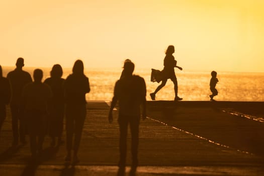 Silhouettes of people at yellow sunset - mother chasing her little baby. Mid shot