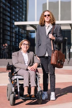 business man and woman using wheelchair posing happy looking at camera outdoors at financial district, concept of diversity and urban lifestyle