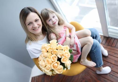 Woman with little girl on her knees holding bouquet of flowers. Mothers day concept