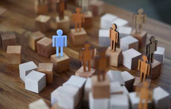 Wooden men on wooden cubes of brown color, one of them is blue. How to stand out among people and be an example to others concept