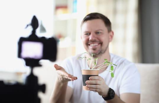 Smiling man demonstrates seedlings on video camera. Introducing home growing blog concept