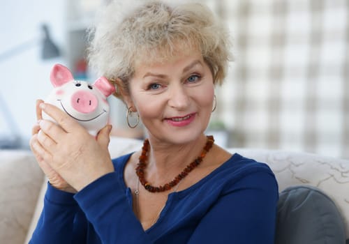Portrait of an elderly woman who holds piggy bank in her hand. Pension fund and deductions concept