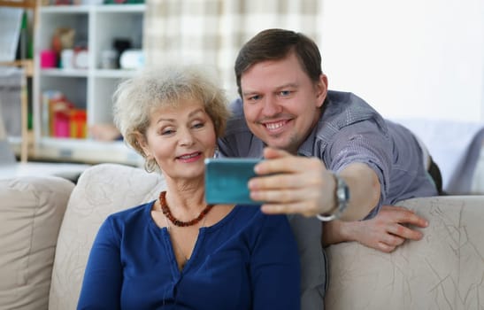 Young man takes selfie on smartphone with his mom. How to teach grandma to use smartphone