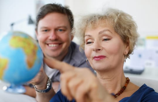An elderly woman and young man looking at globe. Parents and children traveling together concept