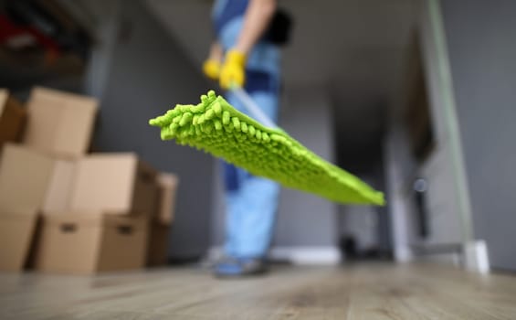 Worker holds mop with green rag for floor. Services of cleaning company concept