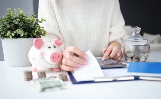 Woman holding checks for purchases in hand and counting on calculator closeup. Home budget planning concept