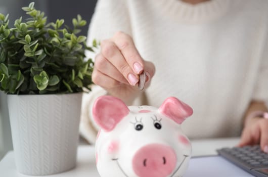 Womans hand throwing coins into piggy bank at home. Family budget concept
