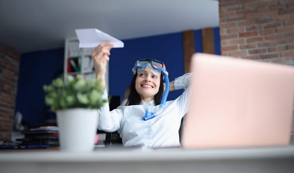 Woman in diving mask launching paper plane at office. Vacation planning concept