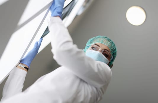 Medic is holding an X-ray in medical protective mask. Doctors fight coronavirus infection concept