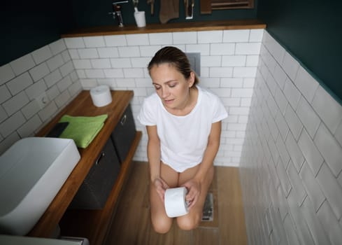Tired woman sits on toilet and holds toilet paper. Bowel problems concept