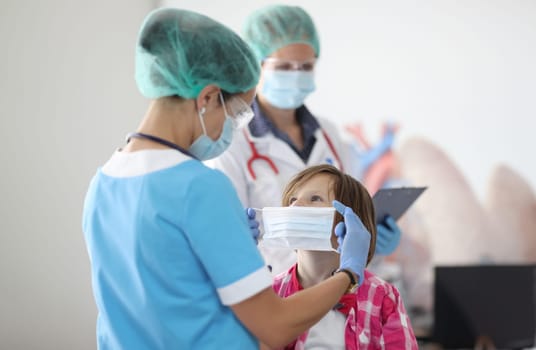 Doctor wearing protective mask puts on mask for little girl. Mask mode for adults and children concept