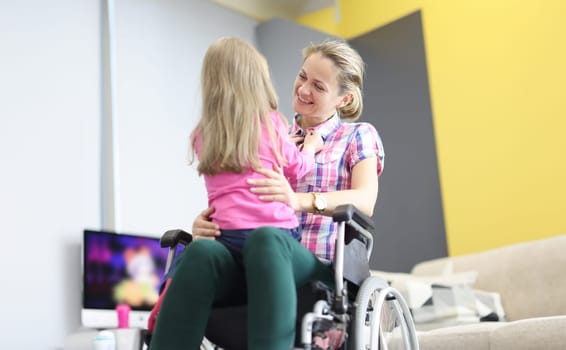 Smiling woman in wheelchair hugs little girl. Parents with disabilities concept