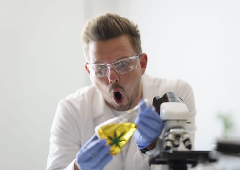 Surprised man holding test tube with yellow liquid. New properties of marijuana concept