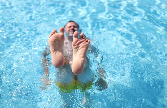 Man shows his feet while lying in pool. Slimming pool exercise concept