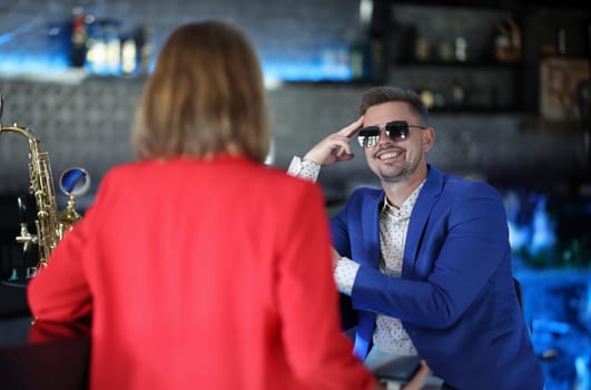 Smiling confident man in sunglasses meets woman near bar counter. Narcissistic personality disorder in men concept