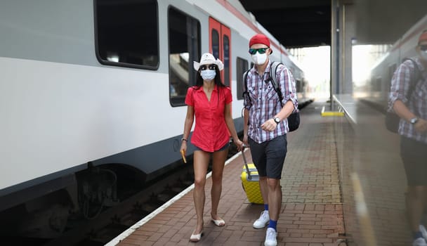 Man and woman in medical protective masks walk along platform of station. Travel rules on trains in coronavirus pandemic concept