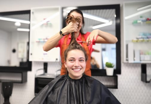 Portrait of smiling woman in hairdressing salon, which master cuts her hair. Women's haircuts and styling in a beauty salon concept