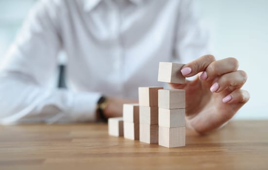 Female hand makes wooden cubes in tower. Planning and building successful business concept